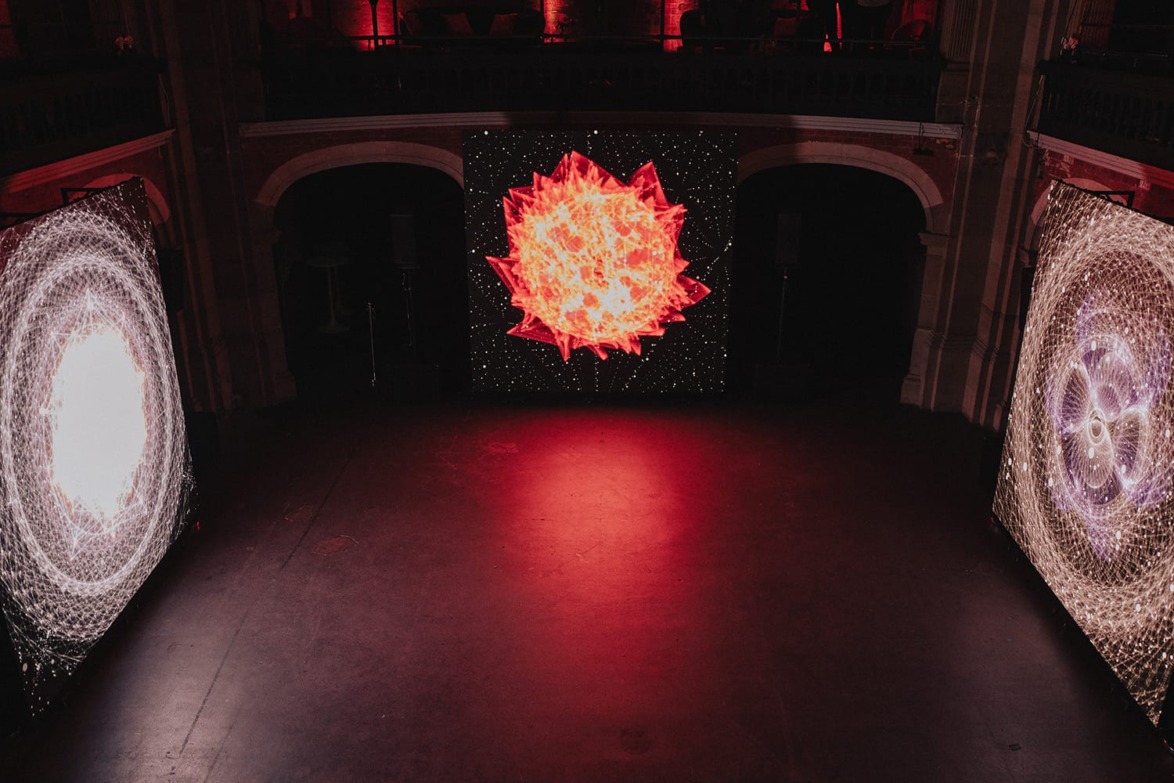 Digital art installation with three illuminated panels featuring intricate, colorful, and dynamic geometric patterns in a dark room.