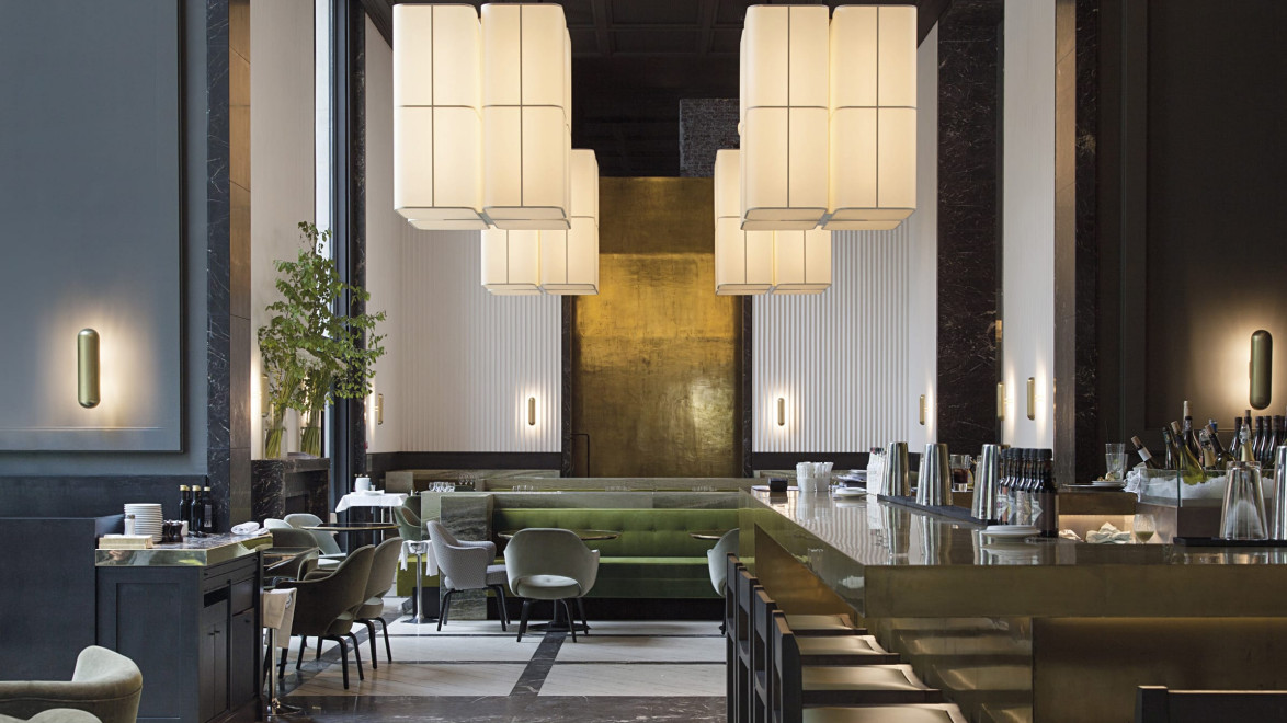 Luxurious modern hotel lobby with elegant lighting, large vertical light fixtures, green seating area, and sleek bar counter.