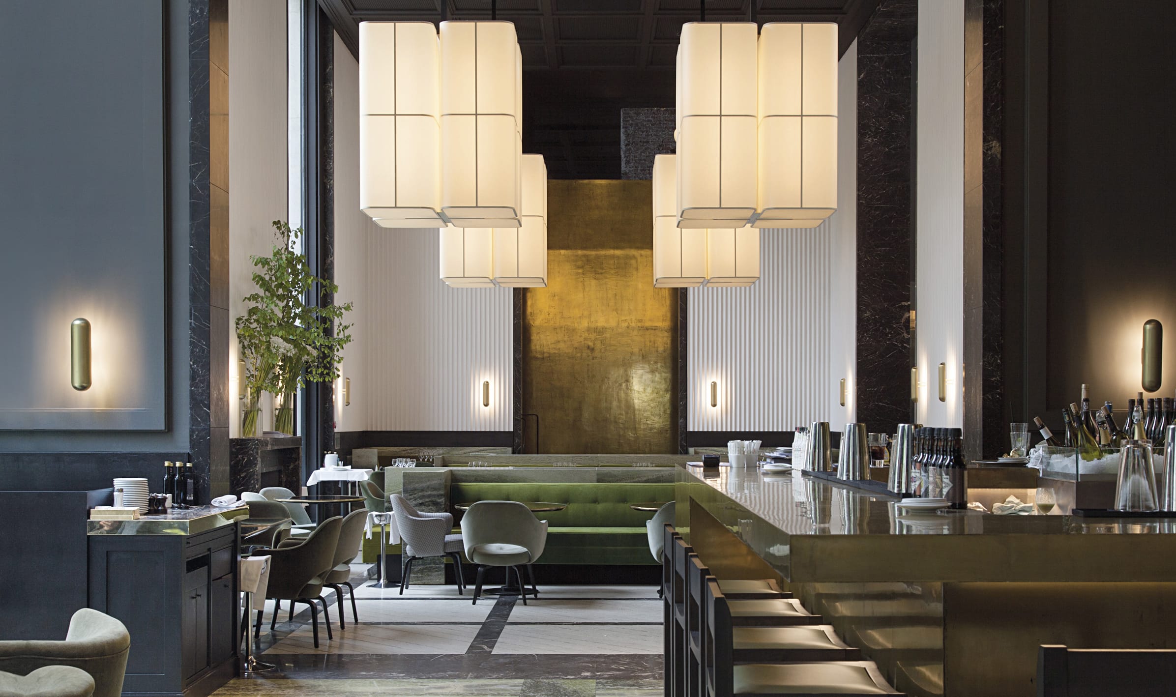 Luxurious modern hotel lobby with elegant lighting, large vertical light fixtures, green seating area, and sleek bar counter.
