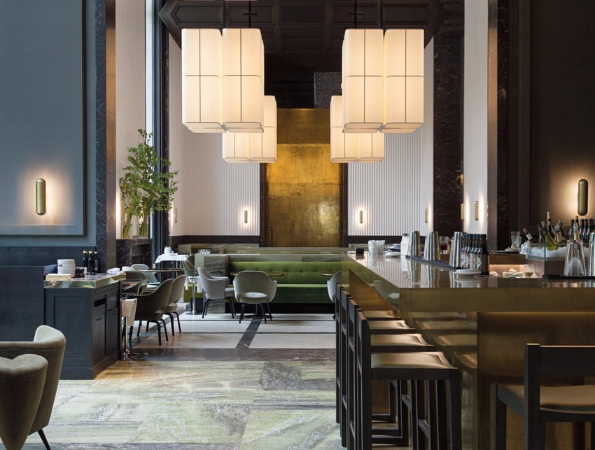 Elegant modern restaurant interior with high ceilings, stylish pendant lights, green seating, and wooden accents.