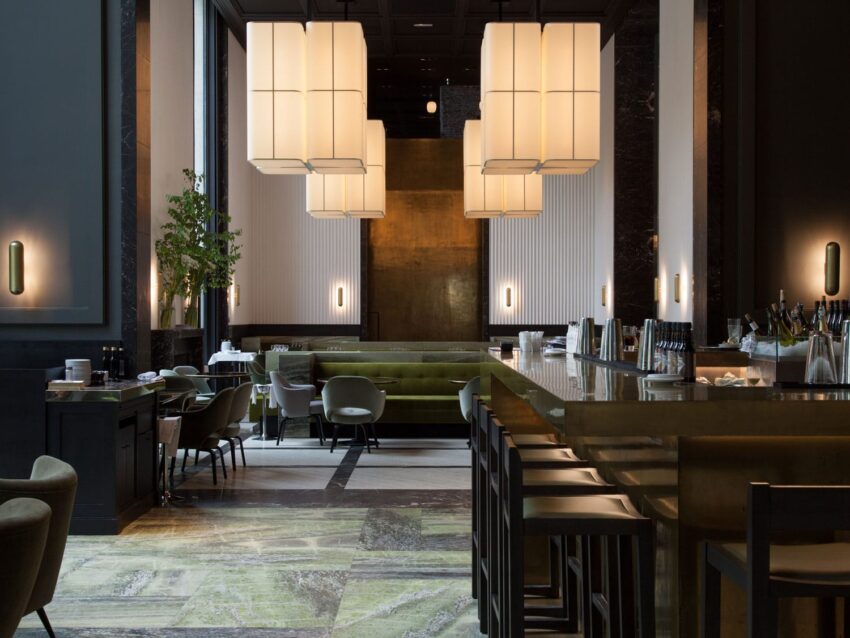 Modern restaurant interior with elegant lighting, green seating, and a sleek bar setup.