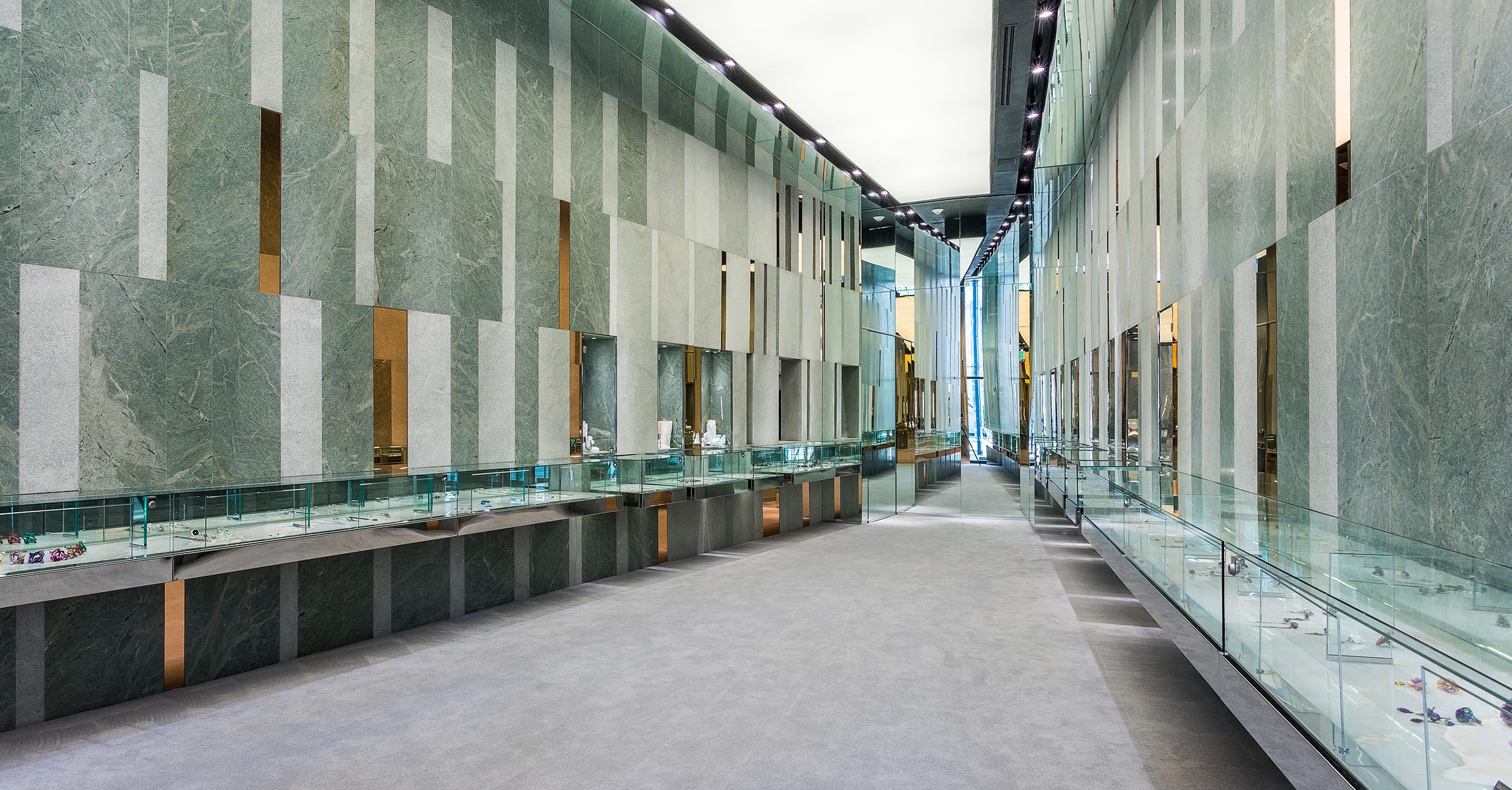 Modern museum corridor with glass display cases, green and white walls, showcasing artifacts under bright lighting.