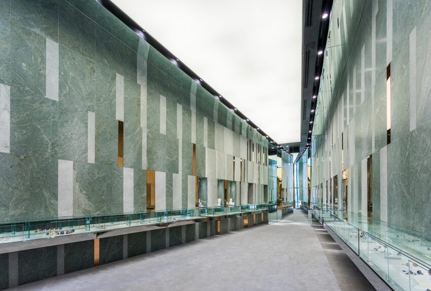 Modern museum corridor with green marble walls, glass display cases, and a polished gray floor creating a sleek, contemporary look.