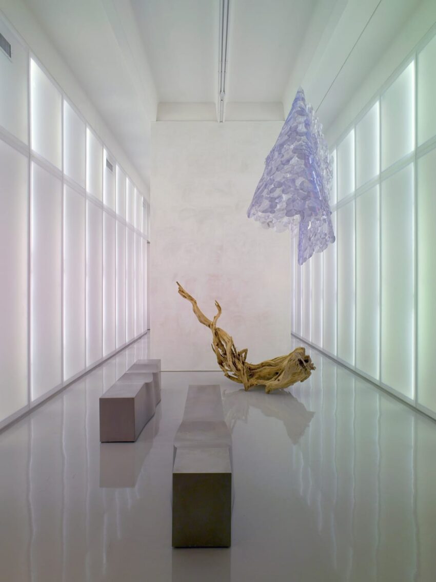 Modern art installation with metal benches, abstract sculpture, and overhead artwork in a minimalist gallery space.