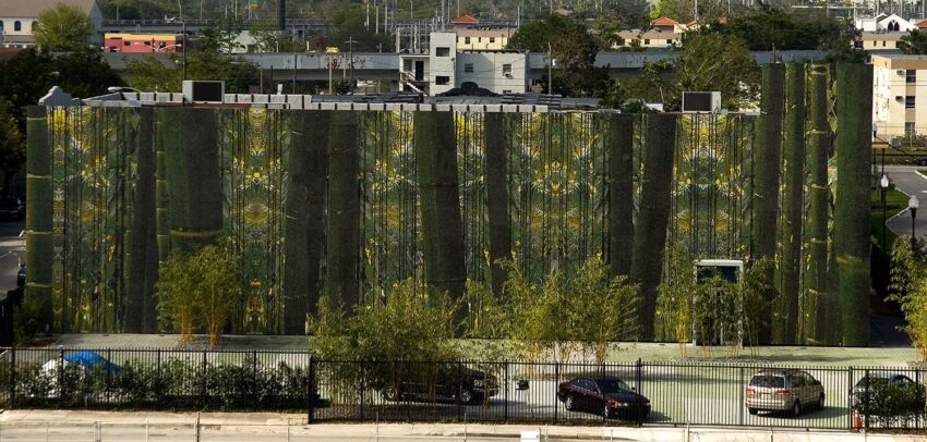 Building covered in green vertical garden with parked cars and surrounding trees.