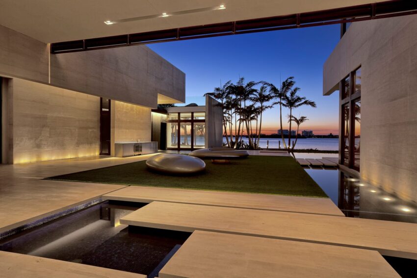 Modern luxury home with sleek architecture, palm trees, and a beautiful sunset over a waterfront view.