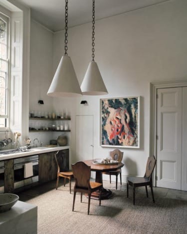 Spacious kitchen with rustic furniture, pendant lights, large window, abstract art on the wall, and a round dining table.