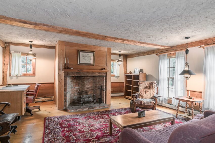 Cozy living room with a rustic fireplace, wooden beams, and a red patterned rug.