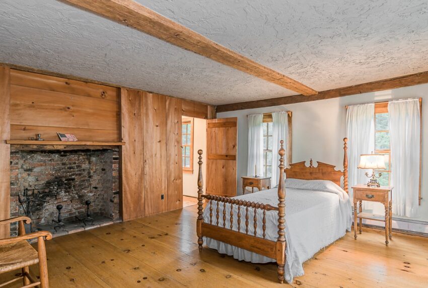 Rustic bedroom with wooden walls, vintage bed, fireplace, and natural light streaming through windows.