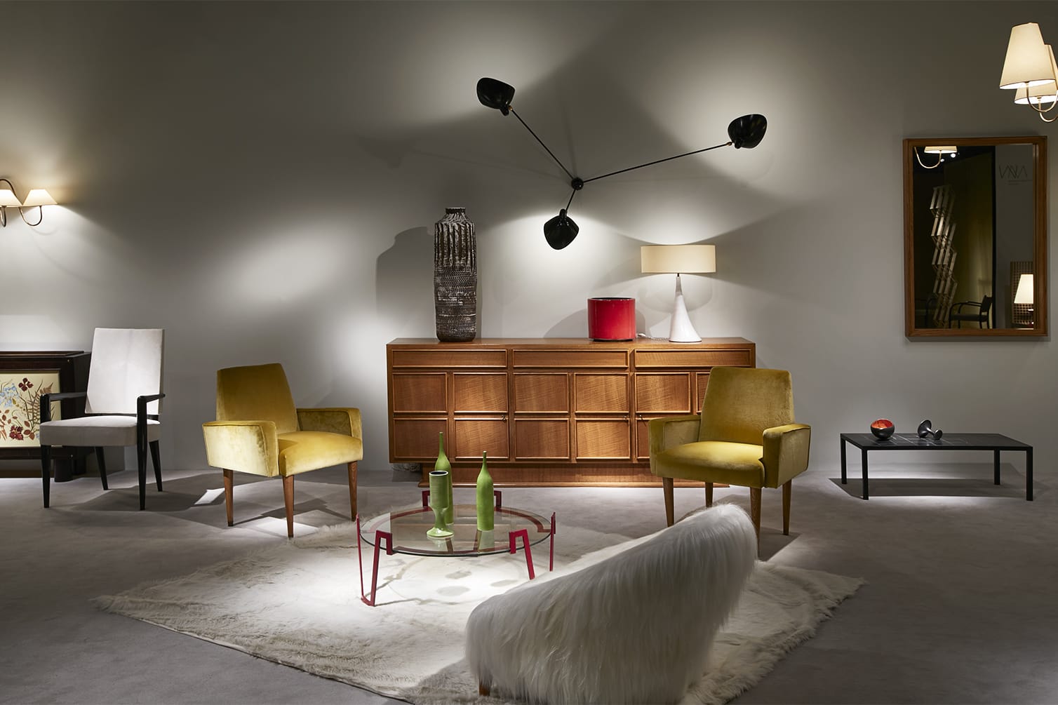 Modern living room with wooden furniture, yellow chairs, wall-mounted lights, and decorative items on a rug.