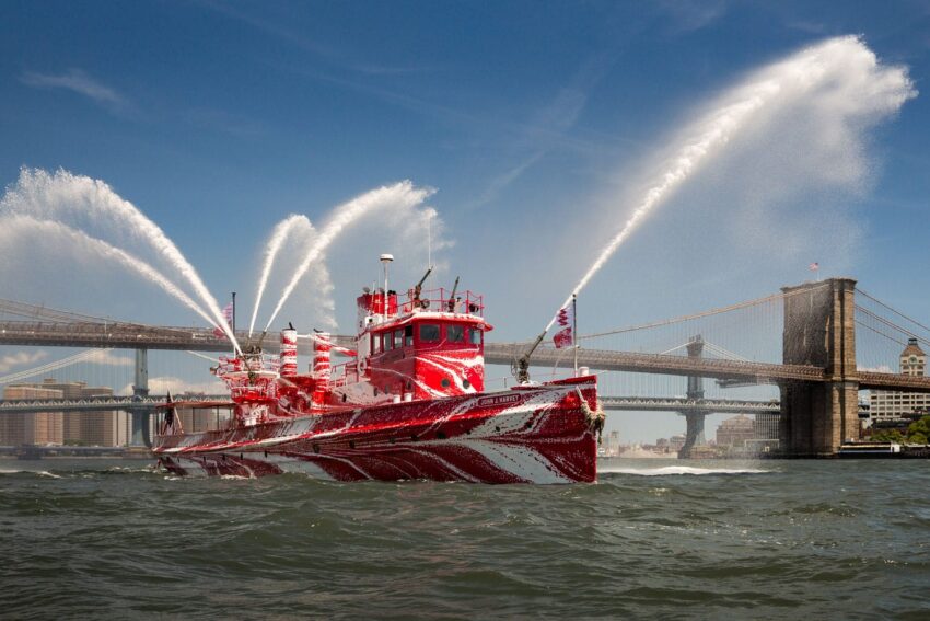 Red fireboat spraying water near a bridge on a sunny day with a clear blue sky in the background.