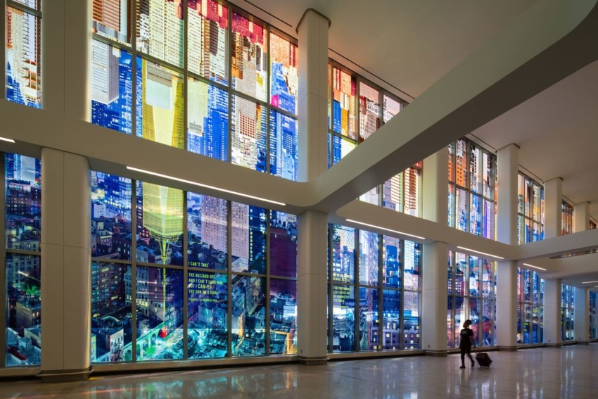 Colorful, abstract stained glass panels in a modern building's interior with a person walking and pulling a suitcase.