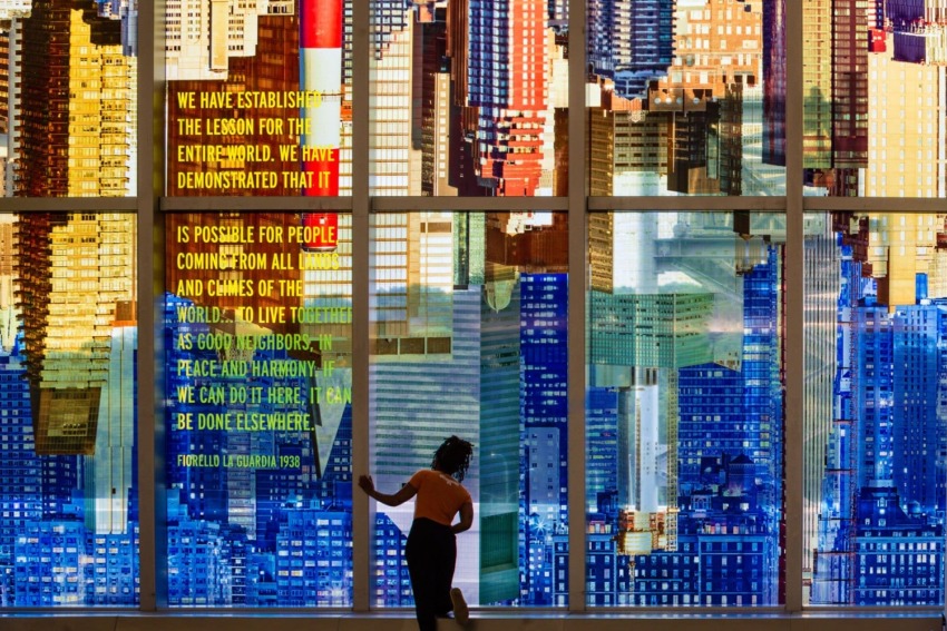 Person stands by large colorful cityscape mural with text about peace and harmony in vibrant urban art display.