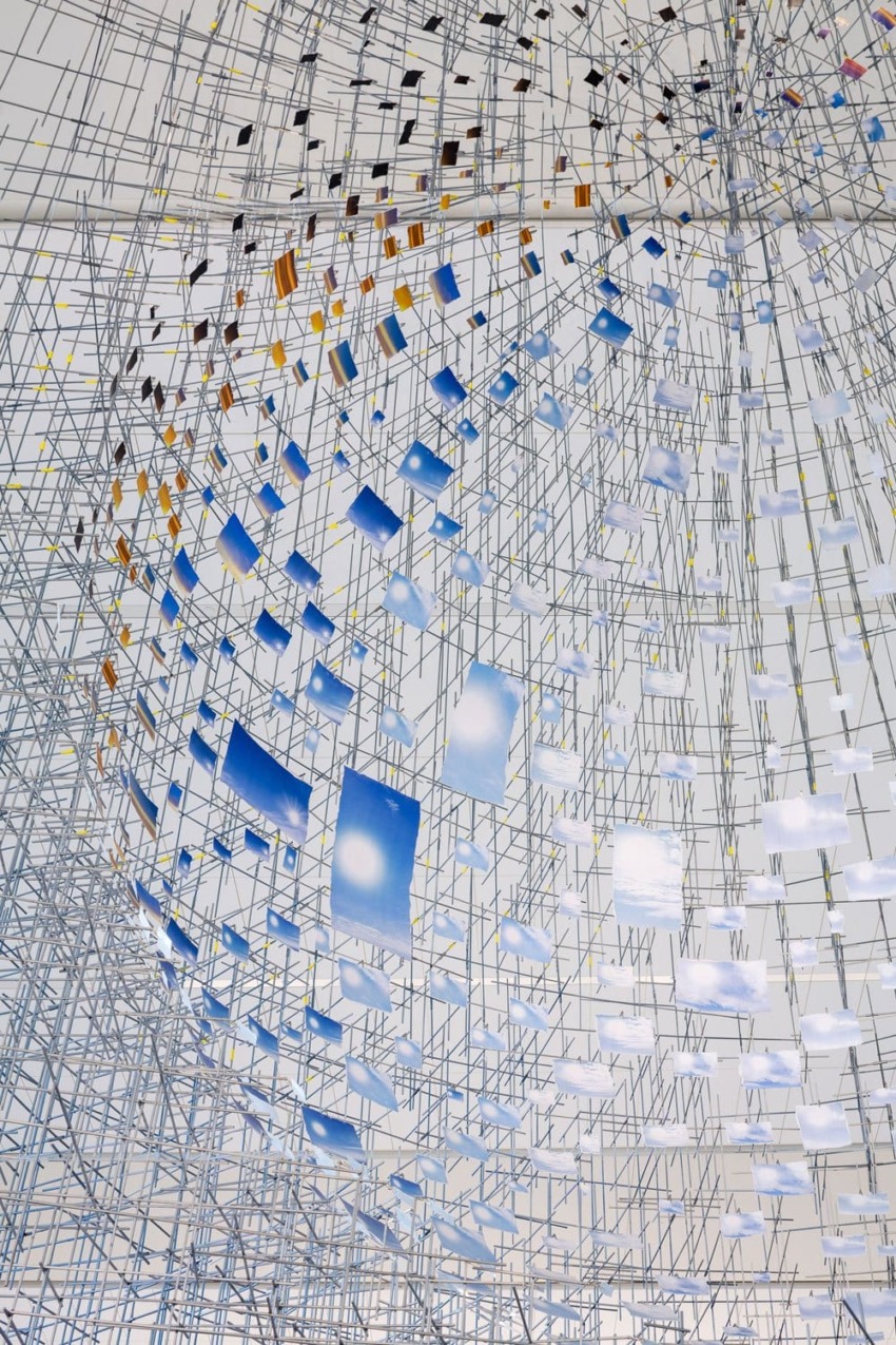 Abstract installation with a grid of metal rods and suspended colored panels, creating a geometric and dynamic visual effect.