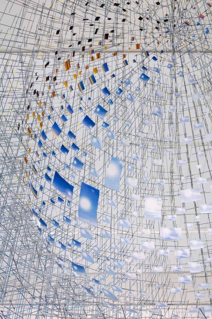 Abstract installation with a grid of metal rods and suspended colored panels, creating a geometric and dynamic visual effect.