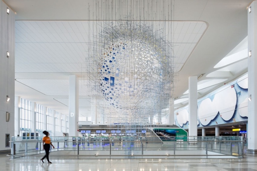 Person walking in a modern airport terminal with a large spherical art installation hanging from the ceiling.