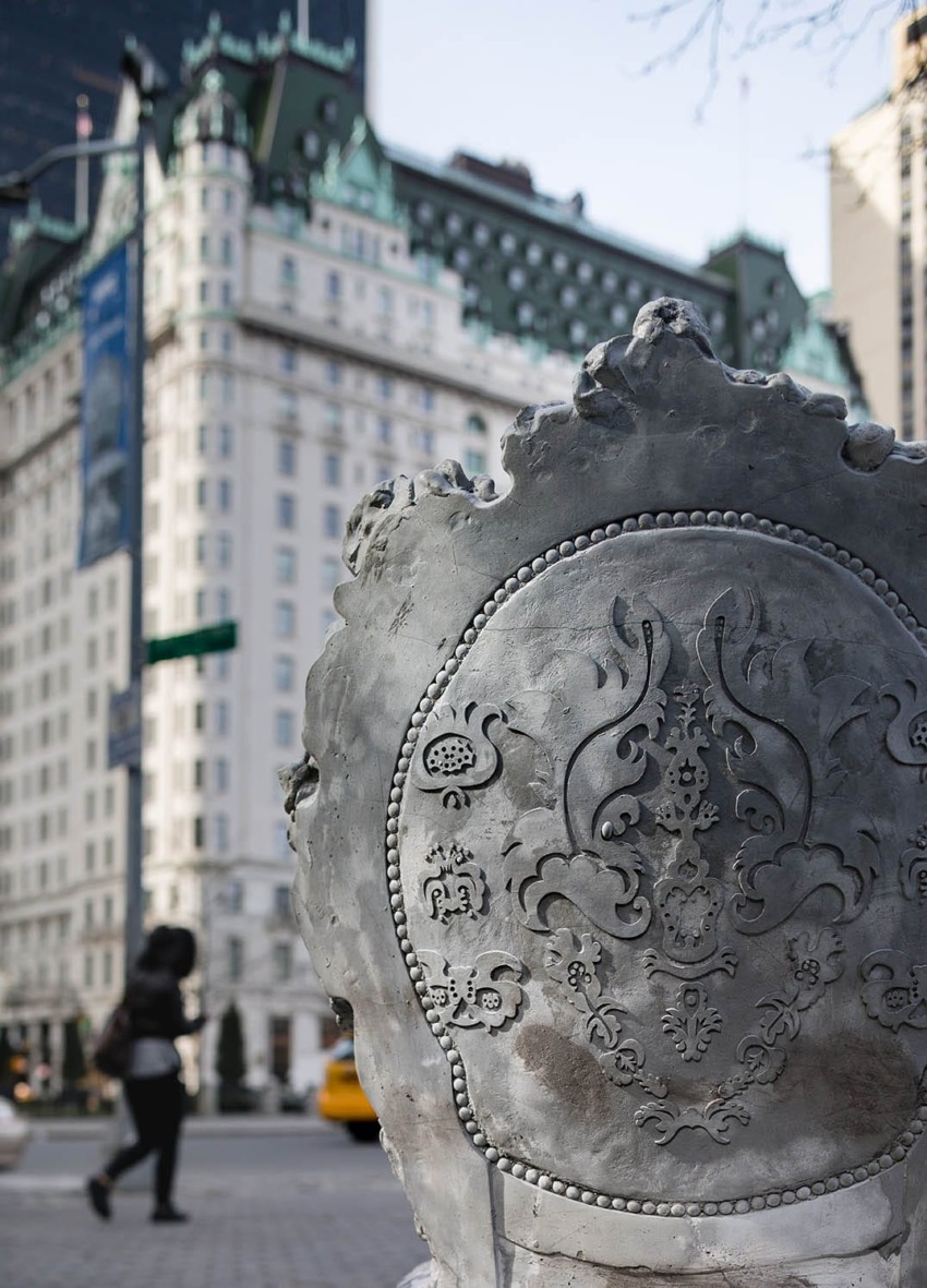 Ornate decorative stonework in focus with a blurred backdrop of a grand, historic building and pedestrians in the background.