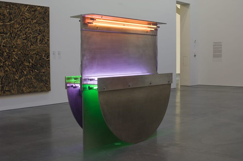 Contemporary art installation with neon lights, metal structures, and vibrant colors displayed in a modern gallery setting.