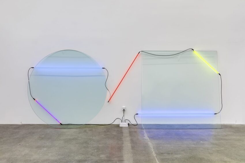 Artistic installation of neon lights on transparent round and square panels mounted on a minimalist white wall.