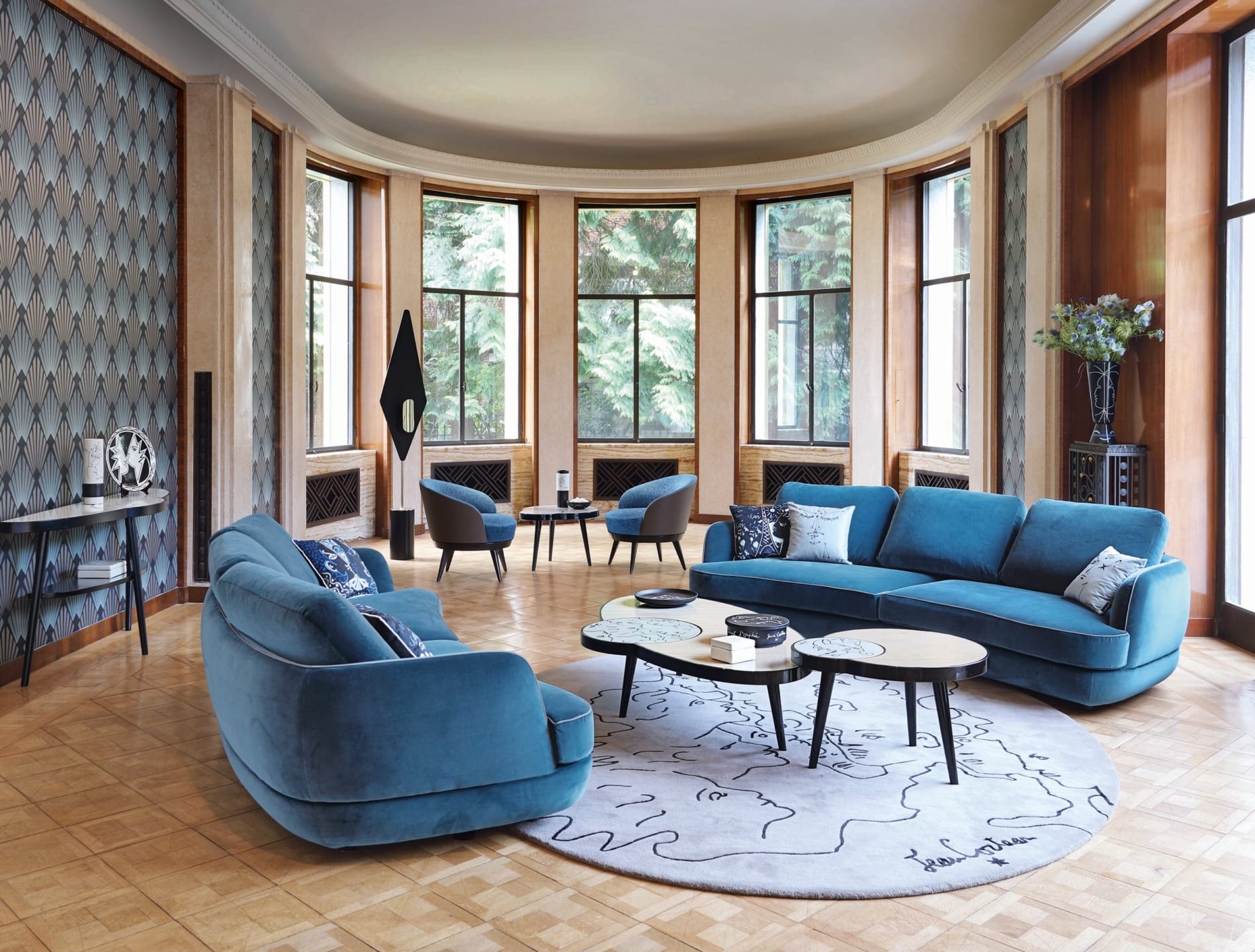 Elegant living room with blue sofas, round coffee tables, and large windows overlooking greenery.