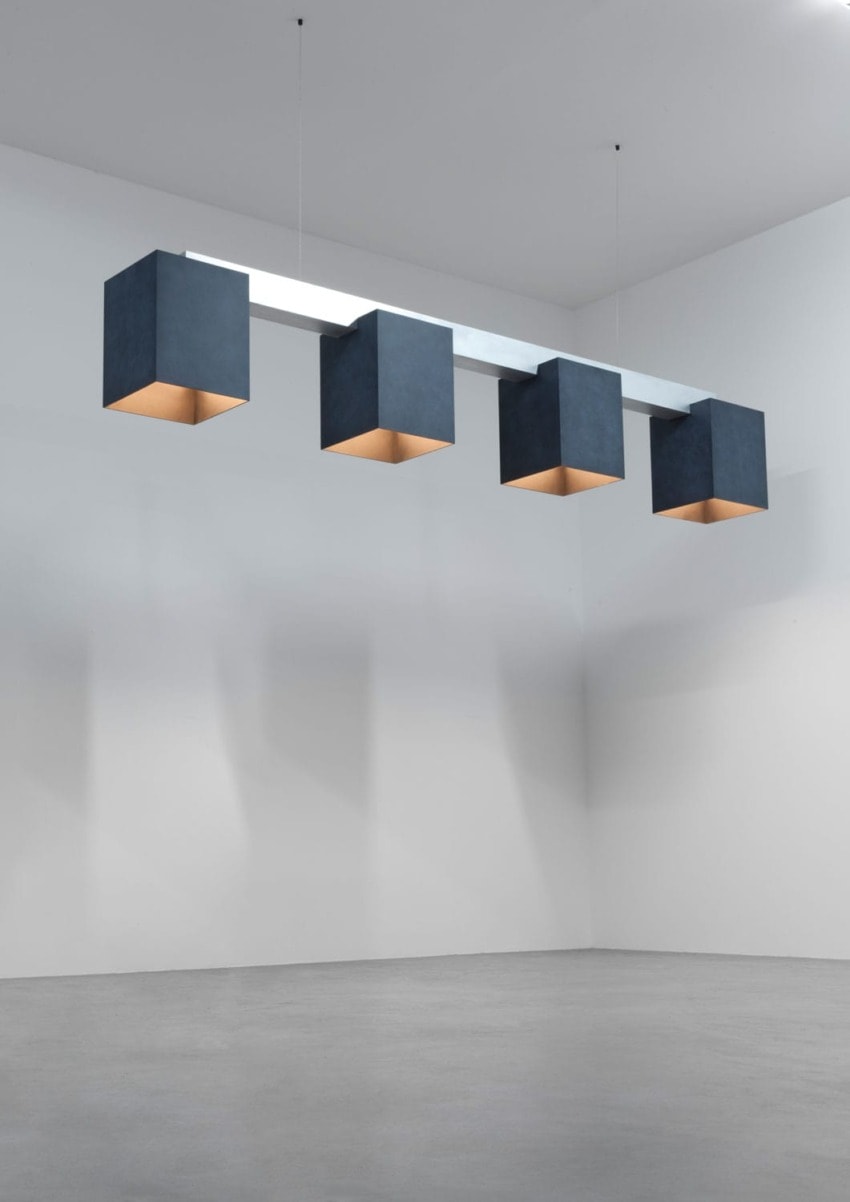 Modern pendant light fixture with five cube-shaped lamps hanging in a minimalist white gallery space.