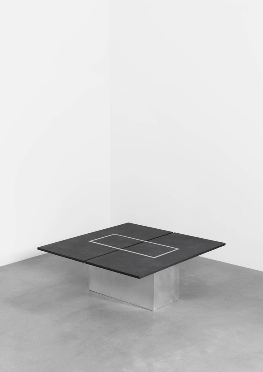 modern minimalist square table with matte black surface on a concrete base in a white-walled room