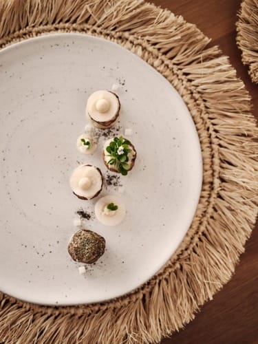Elegant dessert arrangement on a white speckled plate with decorative fringed placemat on a wooden table.