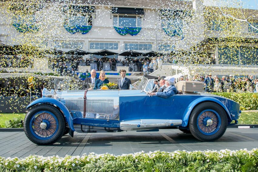 Vintage blue car with four passengers surrounded by gold and silver confetti in front of a festive building.