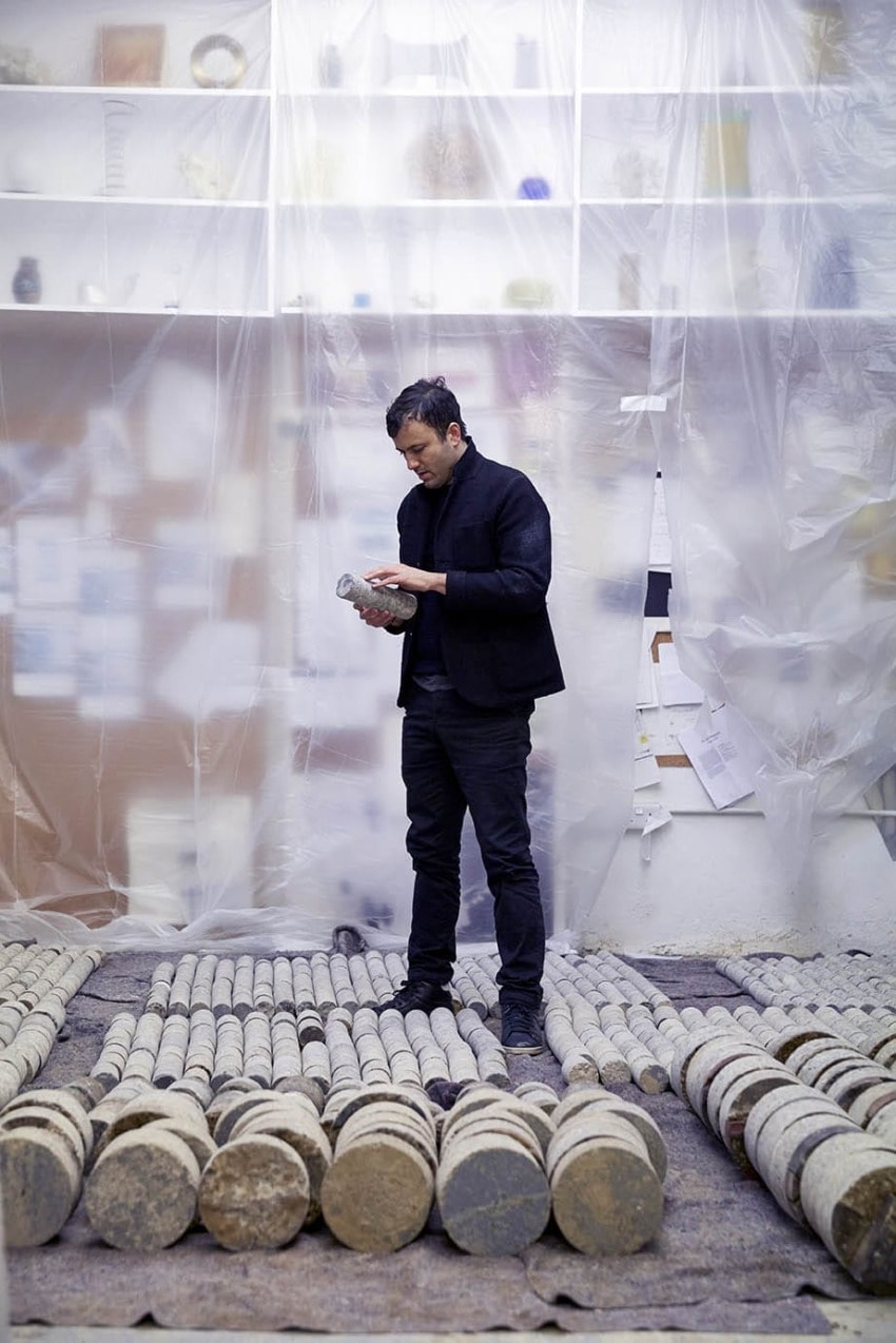 Person examining cylindrical objects in a room with plastic-covered walls and shelves.