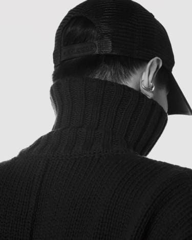 Person wearing a black cap and high-neck sweater, viewed from behind, with a visible ear piercing.