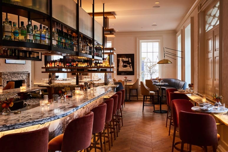 Cozy upscale bar with elegant marble countertops, red velvet barstools, and shelves stocked with various bottles.