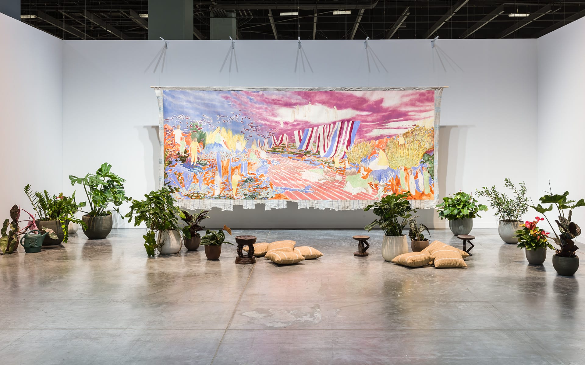Colorful abstract tapestry on a gallery wall surrounded by various potted plants and cushions on a polished concrete floor.