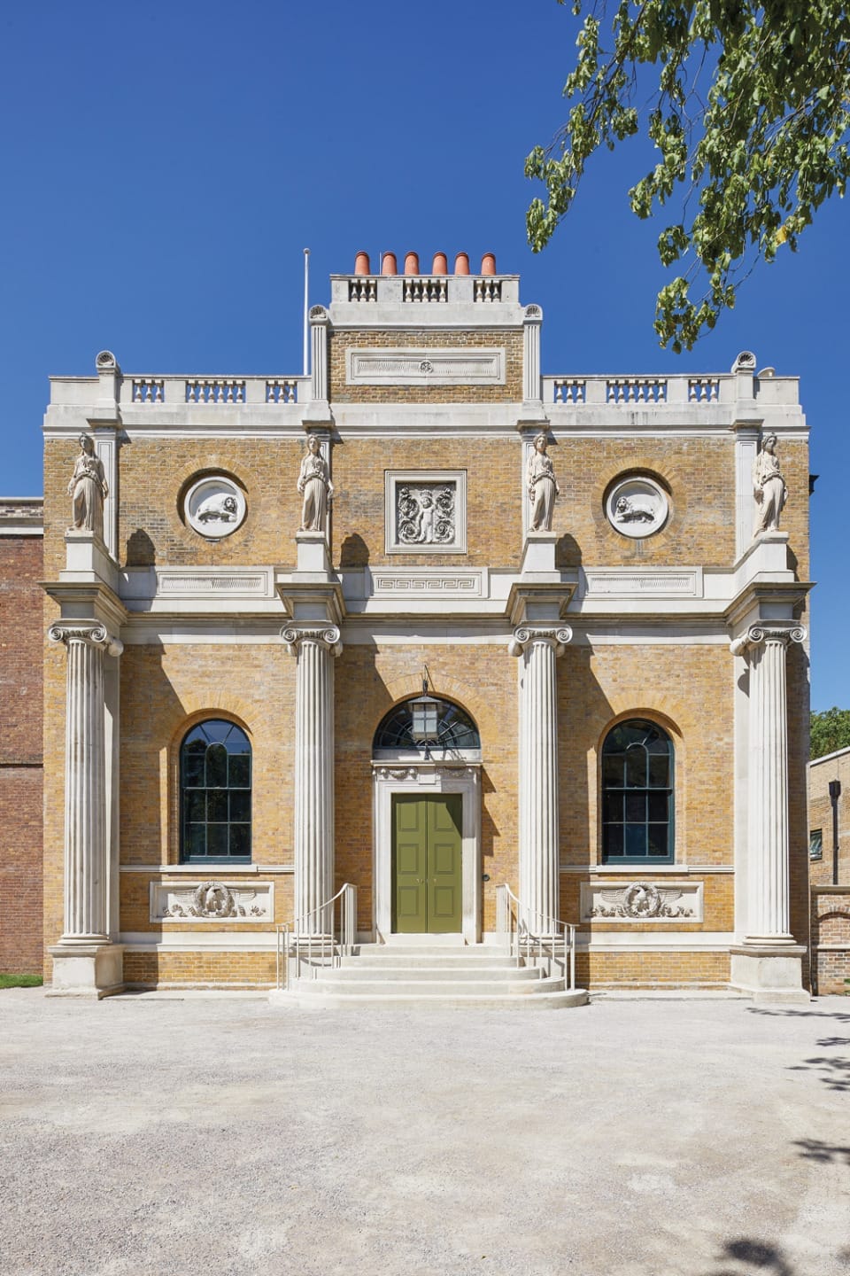 Elegant brick building with classical columns and statues under a clear blue sky.