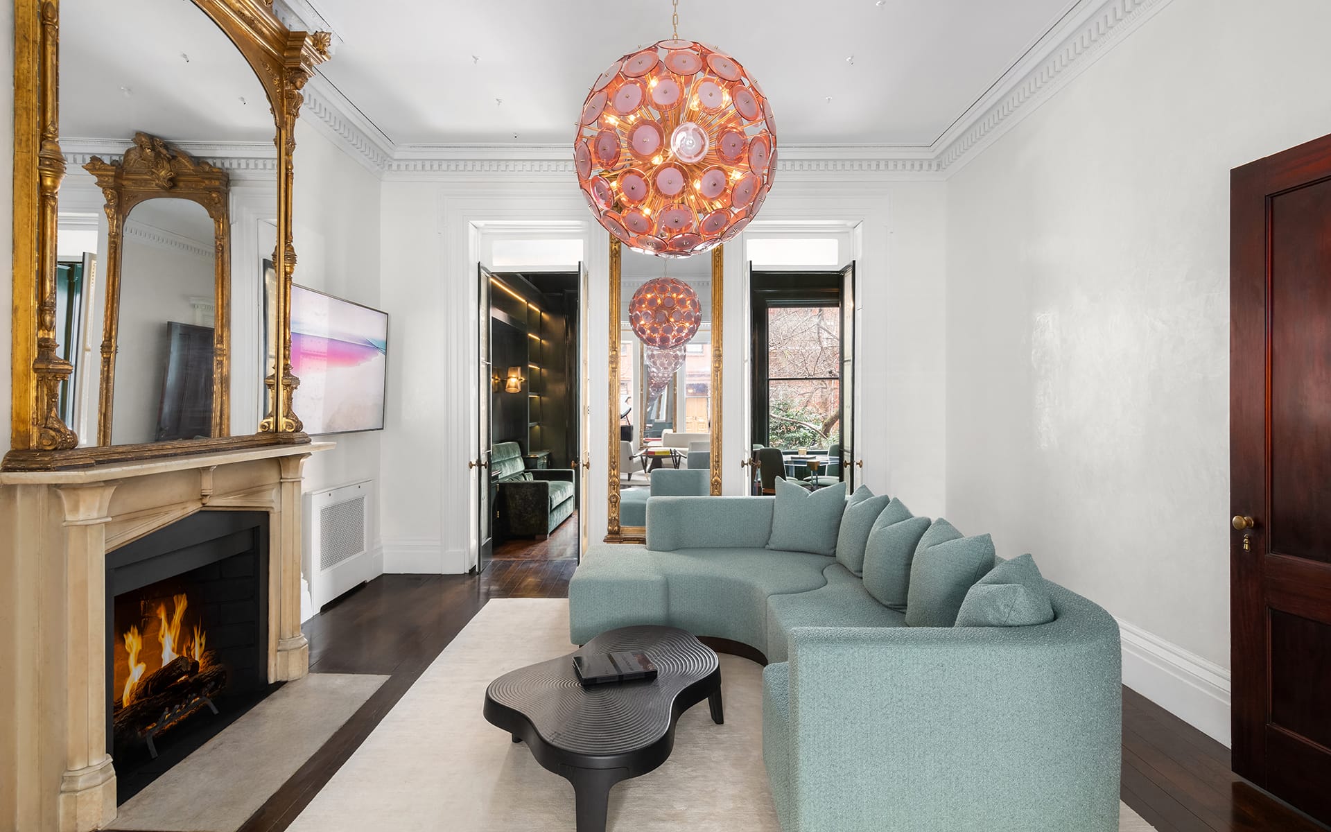 Living room with modern curved sofa, fireplace, large windows, and two pink spherical chandeliers.