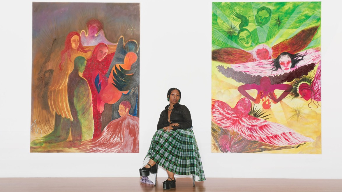 Artist sitting between two large colorful abstract paintings in a gallery setting.