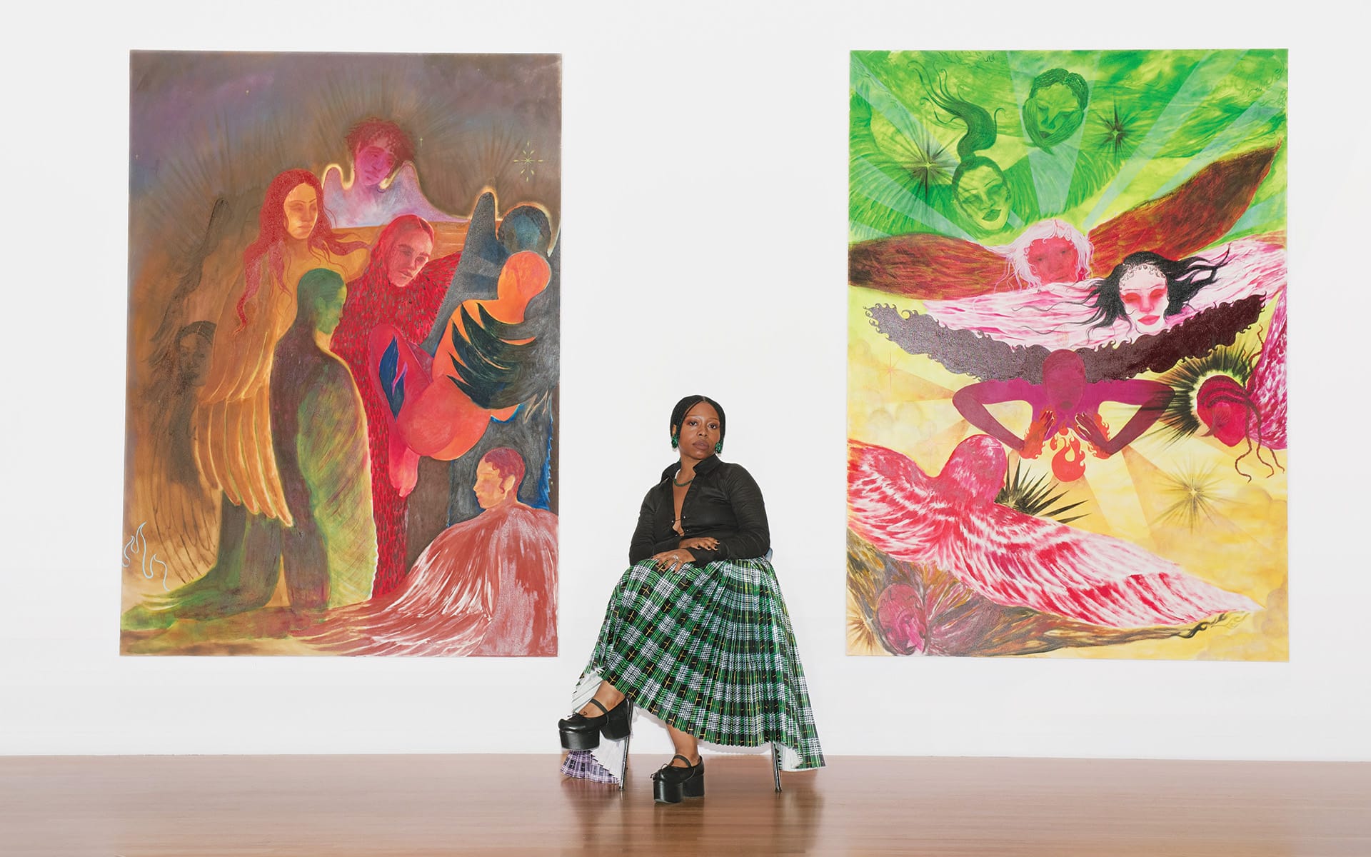 Artist sitting between two large colorful abstract paintings in a gallery setting.