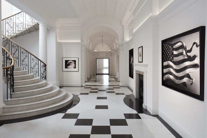 Spacious corridor with black-and-white floor tiles, spiral staircase, and artworks on walls. Elegant and minimalist interior design.