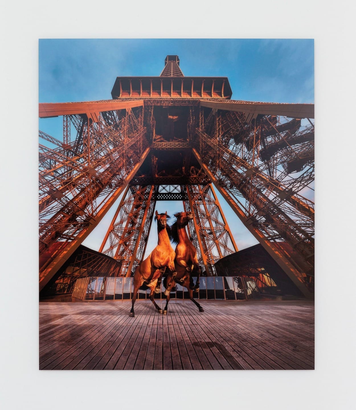Two brown horses standing under the Eiffel Tower with a clear blue sky in the background.