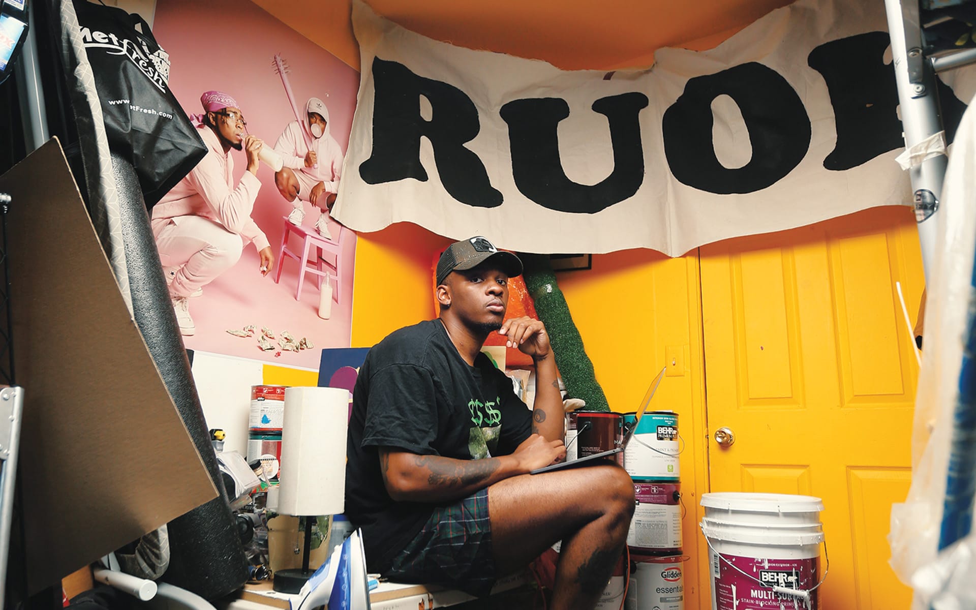 Person sitting in a colorful room with art supplies, surrounded by painting materials and a large banner on the wall.