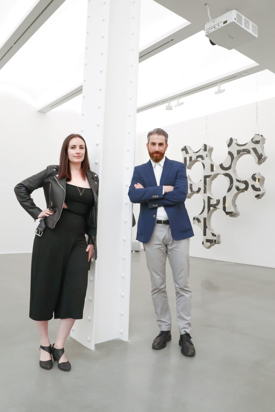 two people standing in a modern art gallery with abstract sculptures hanging in the background