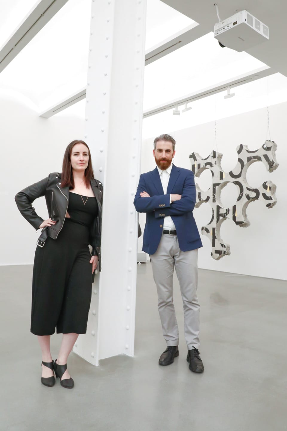 two people standing in a modern art gallery with abstract sculptures hanging in the background