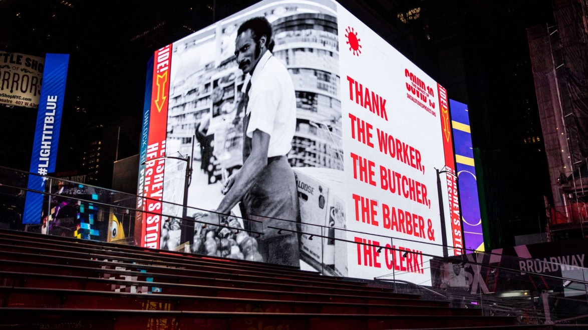 Digital billboard showing an image of a worker with text thanking workers like butchers, barbers, and clerks in Times Square.
