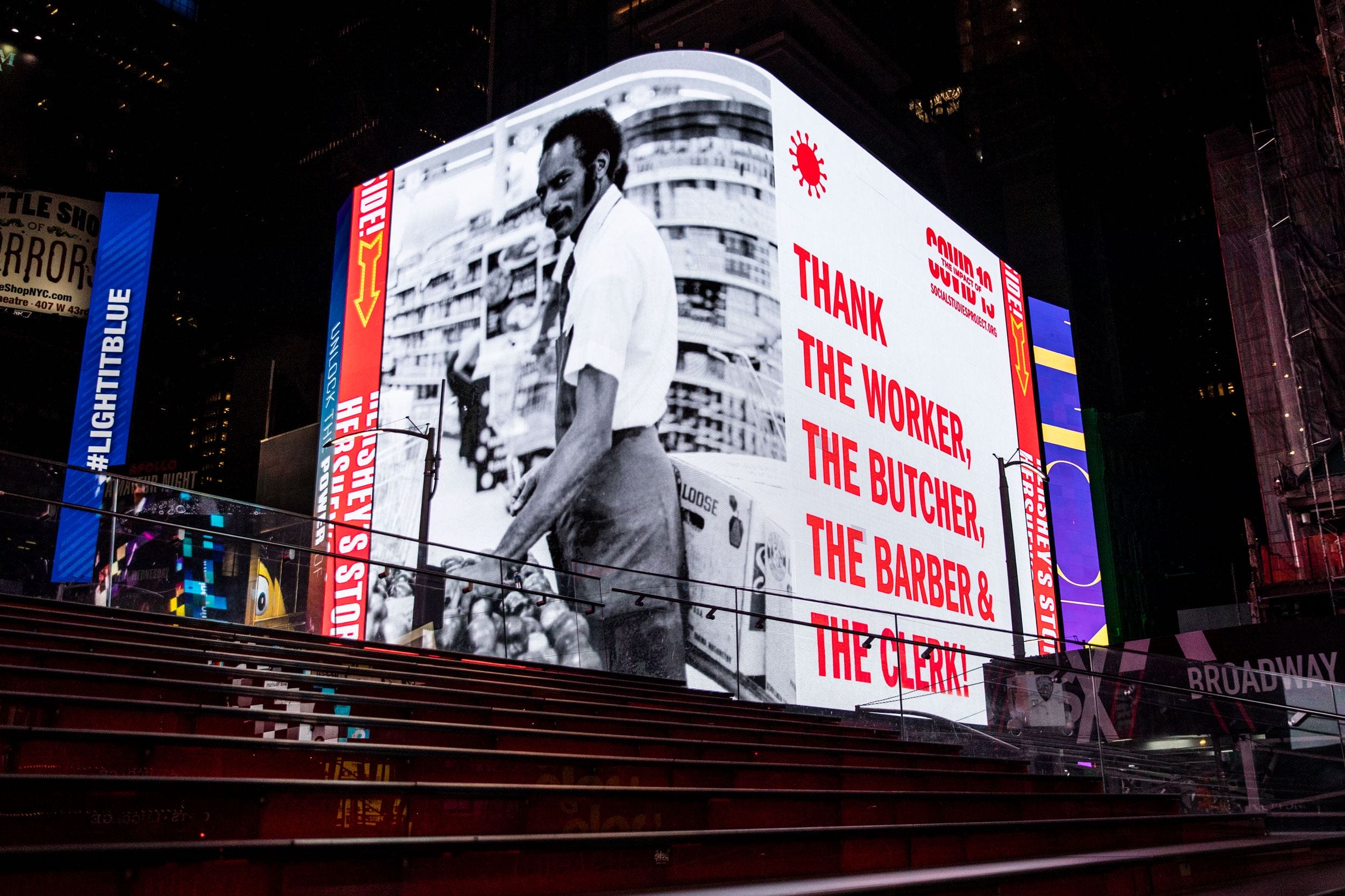 Digital billboard showing an image of a worker with text thanking workers like butchers, barbers, and clerks in Times Square.