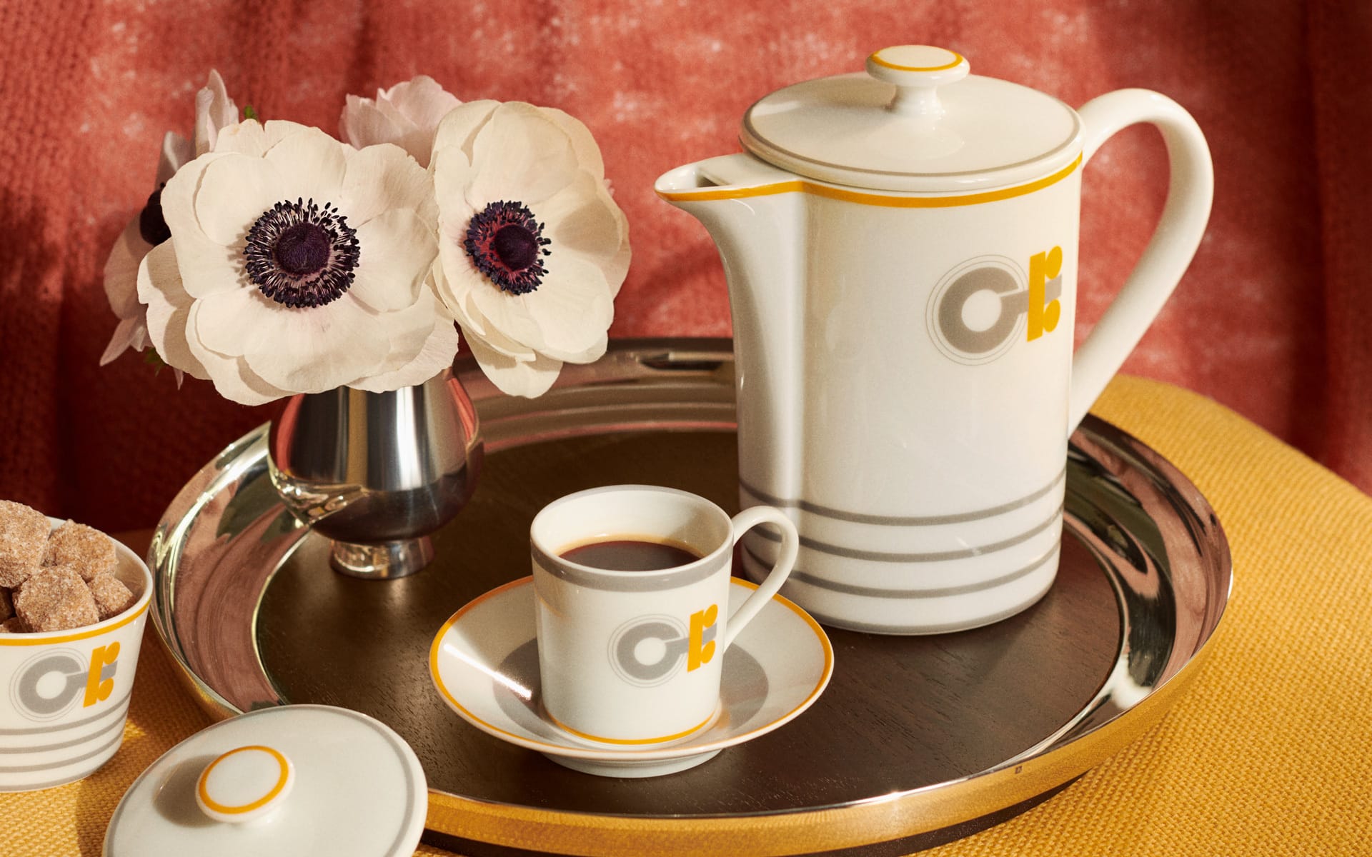 Elegant tea set with a white teapot, matching cup on a saucer, sugar bowl, and white flowers on a silver tray.