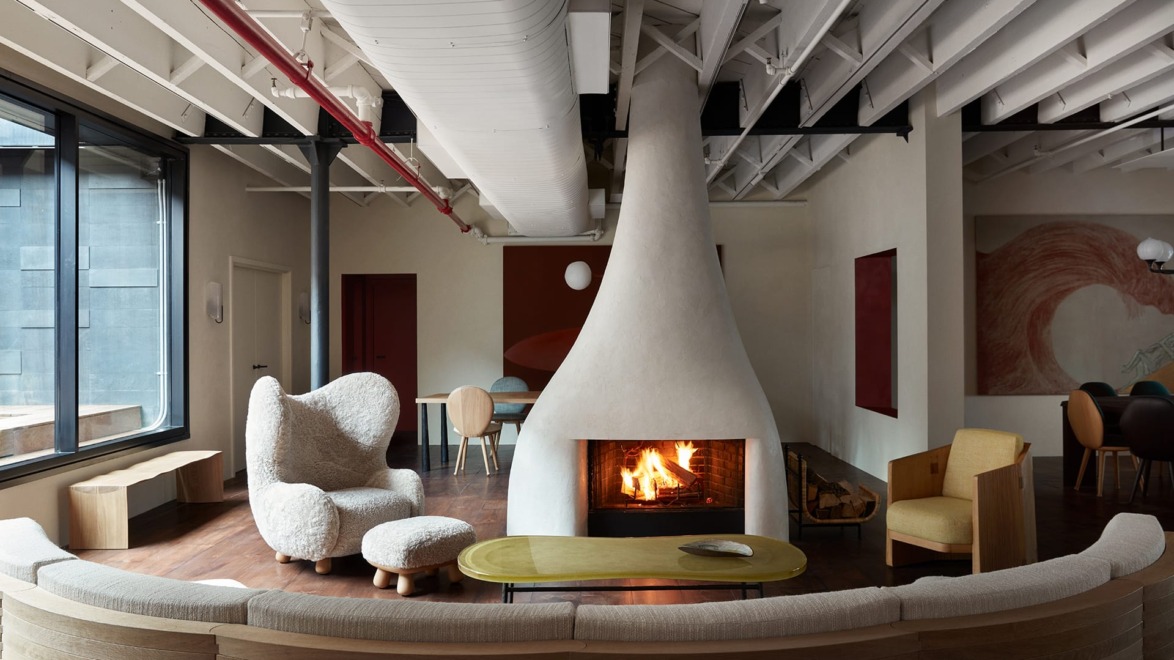 Modern living room with unique cone-shaped fireplace, plush chairs, wooden table, and exposed ceiling beams.