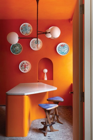 Modern kitchen with orange walls, unique pendant light, terrazzo countertop, and decorative plates on the wall.