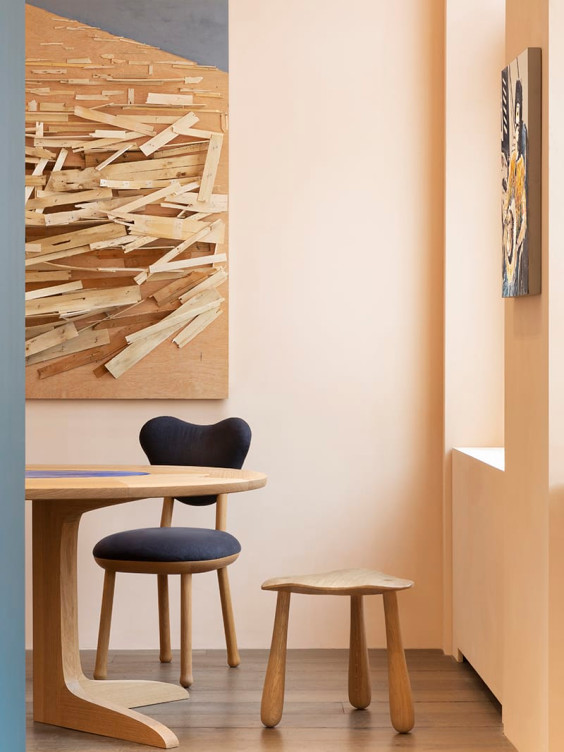 Modern minimalist room with abstract art, wooden table, black chair, and small wooden stool on a wooden floor.