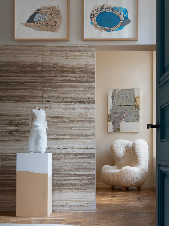 Modern interior with a fluffy chair, abstract art on walls, and a sculpture on a pedestal in a well-lit space.