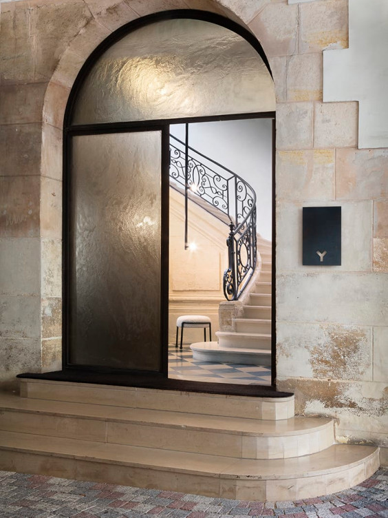 Elegant stone staircase with ornate railing visible through an arched glass doorway in a stone building.