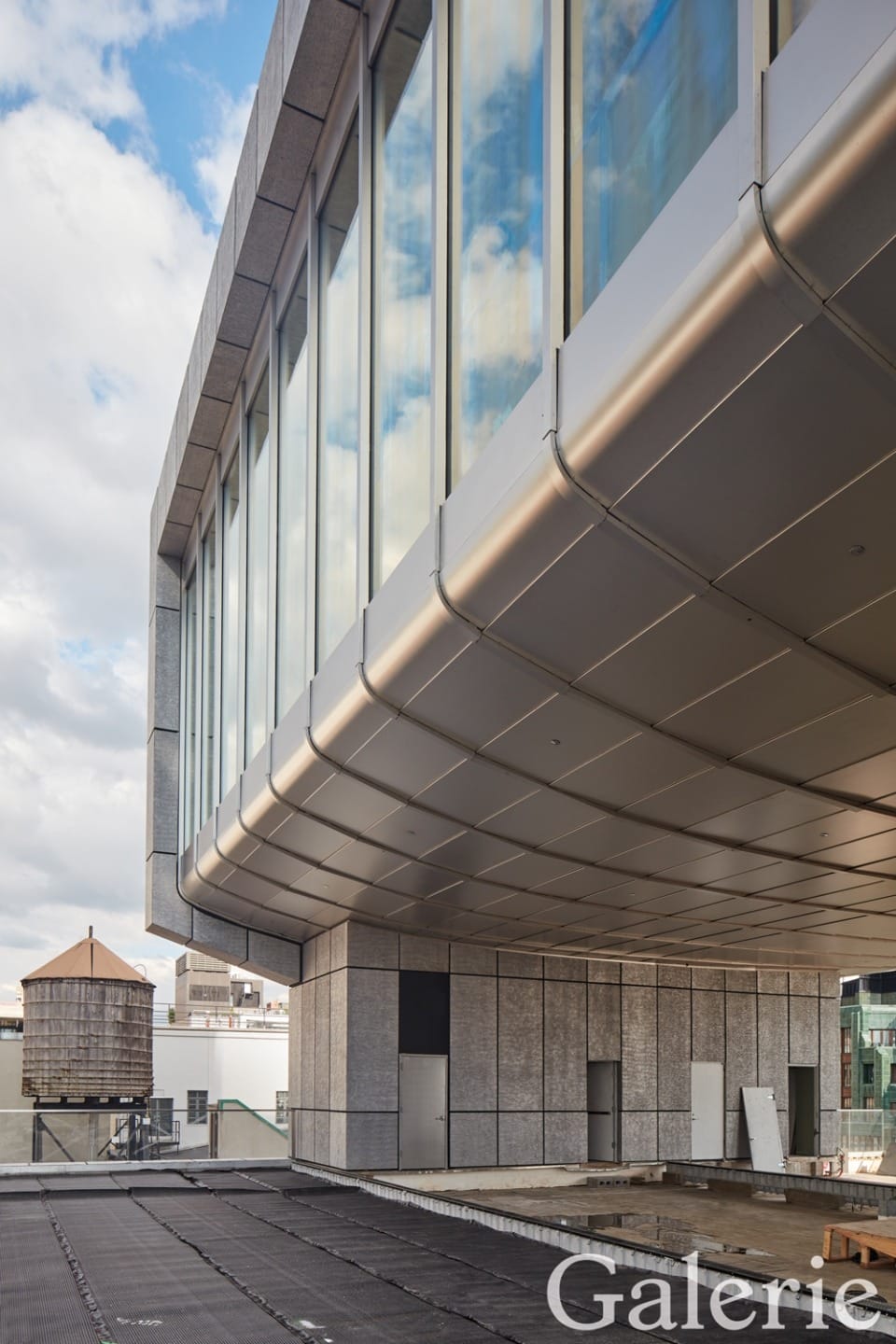 Modern building exterior with large windows and sleek design, overlooking an urban setting with a water tower nearby.